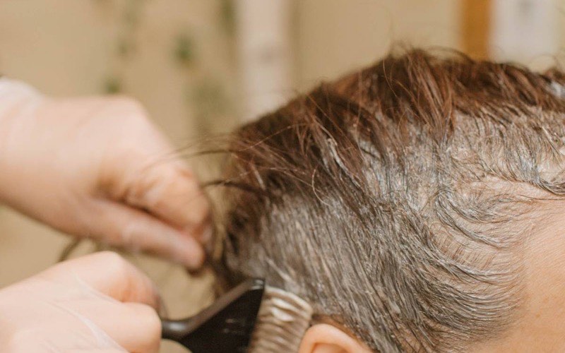 A stylist applying colour at the root with a tint brush during a colour appointment