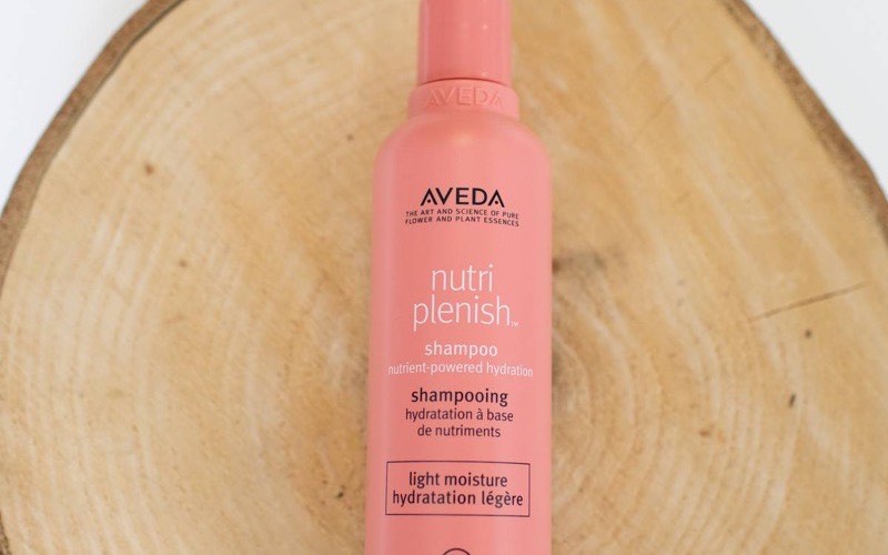An AVEDA haircare bottle photographed on a round wooden slice