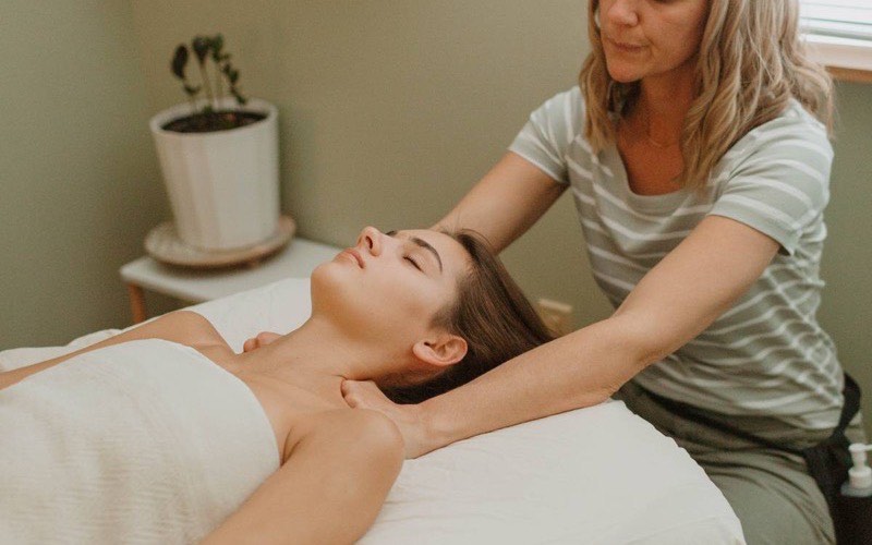 A massage therapist working gently at a client's neck and head while she lies on the table
