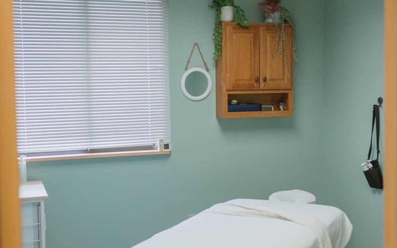 A prepared massage room with a made table, warm wood cabinet and soft light