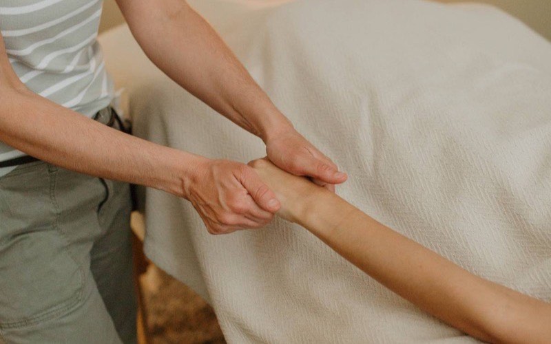 A massage therapist working along a client's arm in a warmly lit treatment room