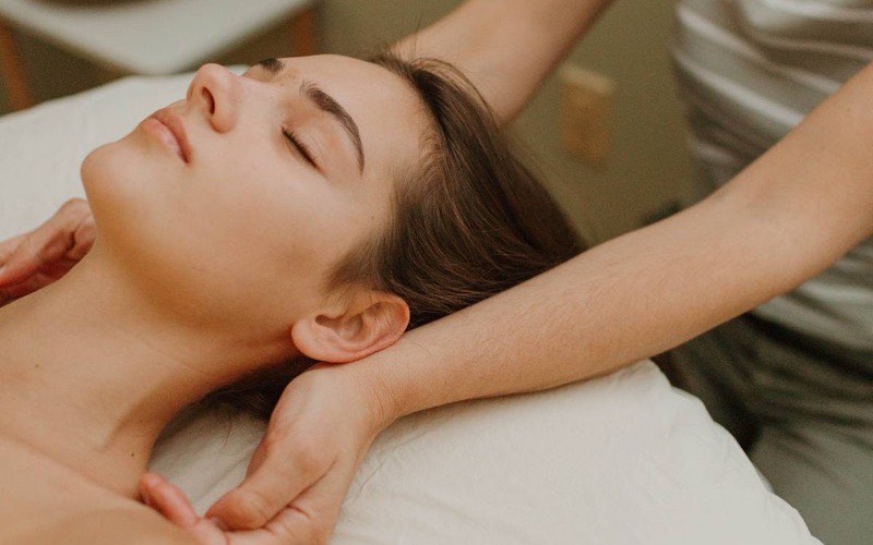 A massage therapist working along a client's neck and shoulder while she lies on the table