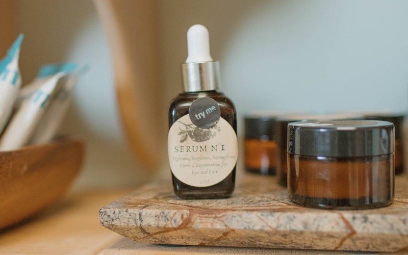 A dropper bottle of oil and a small amber jar arranged on a wooden shelf