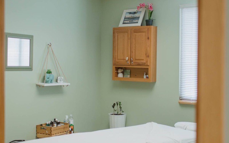 A quiet treatment room with a made-up massage table and warm wooden cabinetry