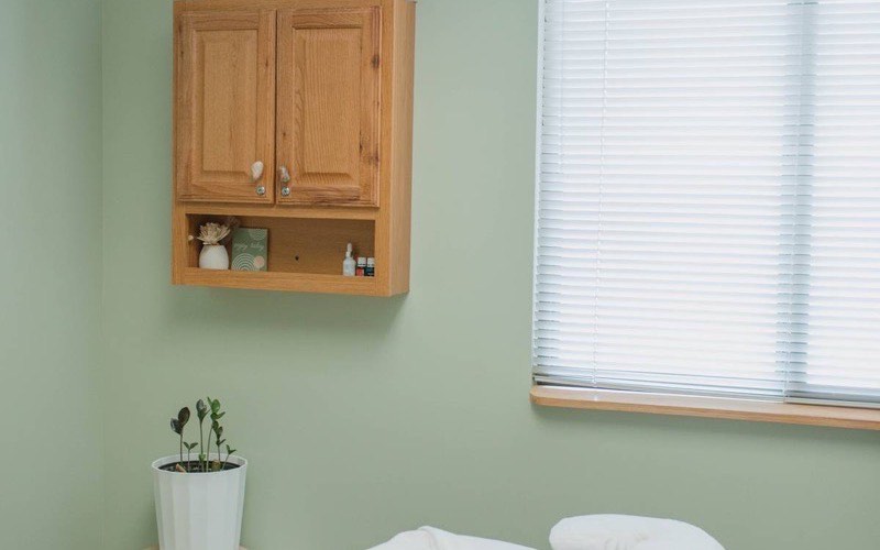 A calm treatment room with soft green walls, a made table and natural light